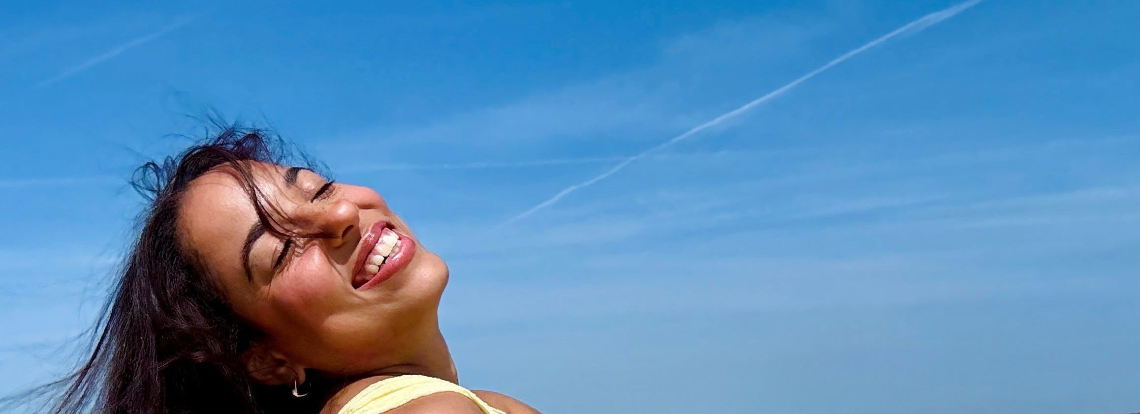 Woman in a yellow outfit lying on a beach with a clear blue sky.