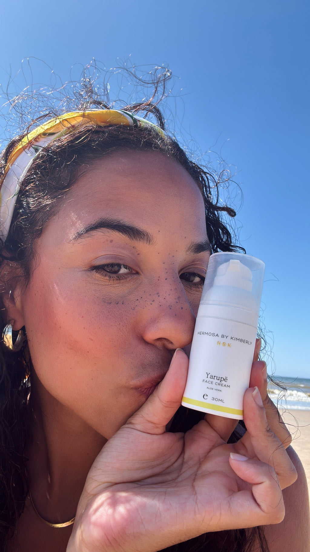Woman holding a skincare product psoriasis, dry skin and sensitive skin with a beach in the background